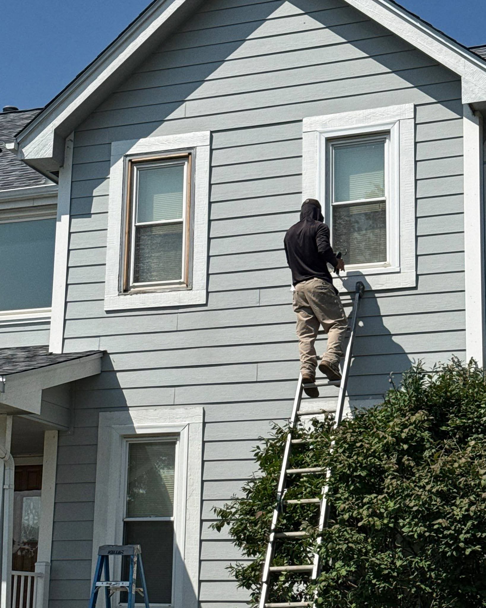 Vinyl Siding Omaha Siding installer on a ladder working on light blue vinyl lap siding and white window trim on an Omaha home
